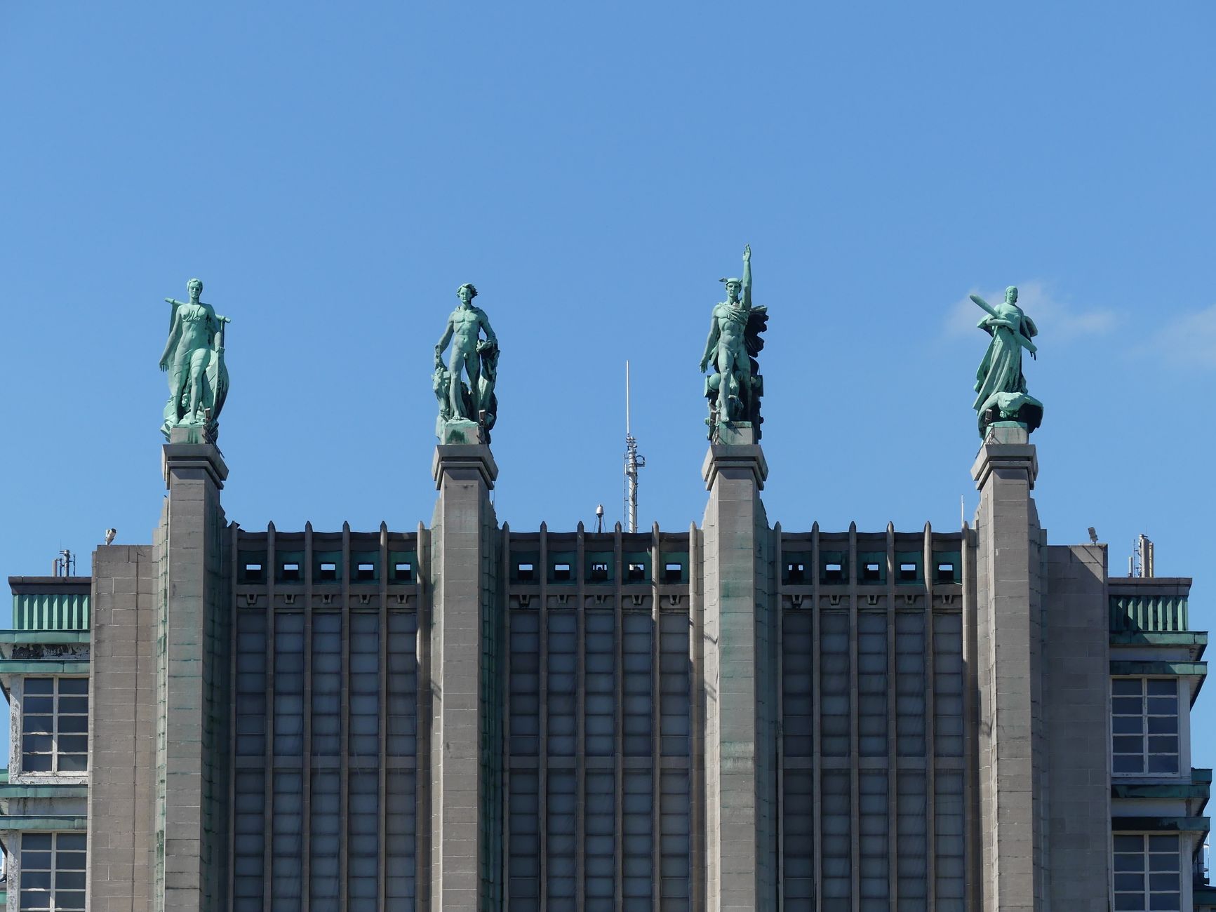 Close up view of Art Deco statues atop the Brussels Exhibition Center under clear blue sky