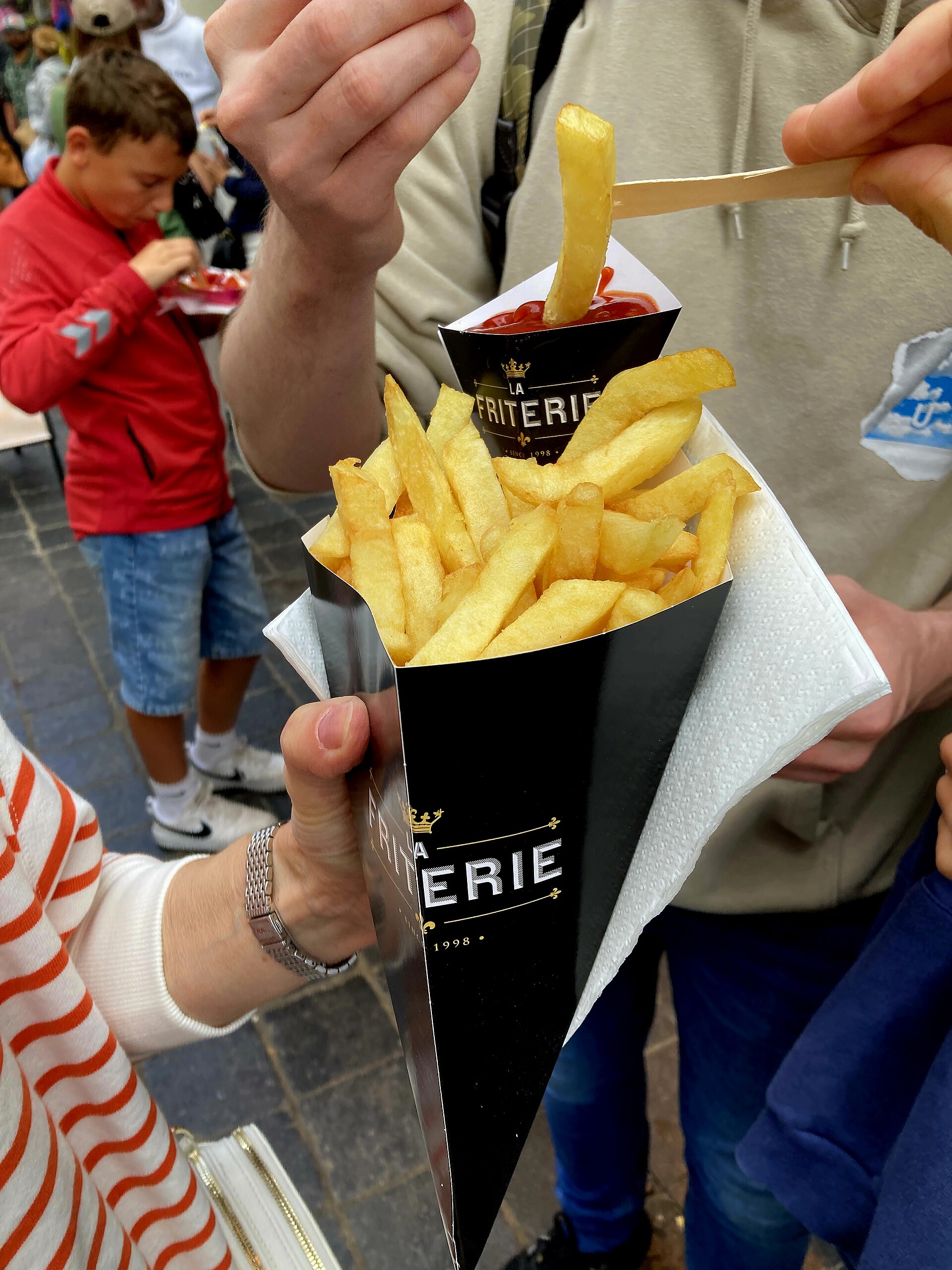 A cone of Belgian fries being handed over
