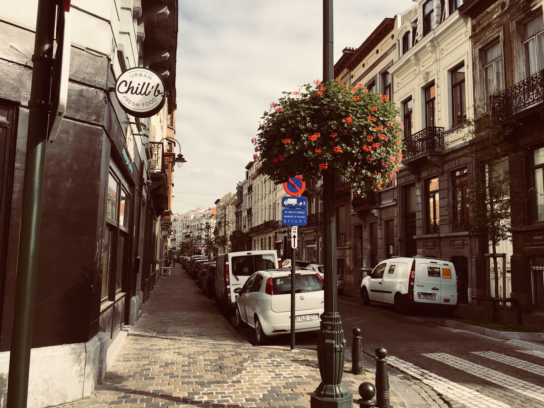 Cobblestone street in Brussels lined with historic buildings and colorful flowers. Daytime view